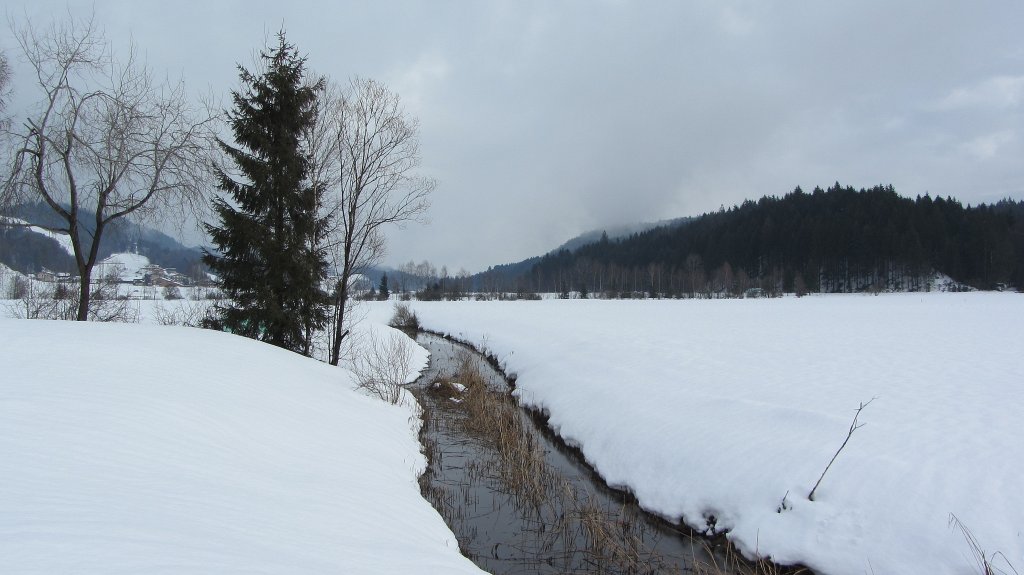 Blick auf ein Schneefeld und einen kleinen Bach bei Kramsach am 22.1.2012.