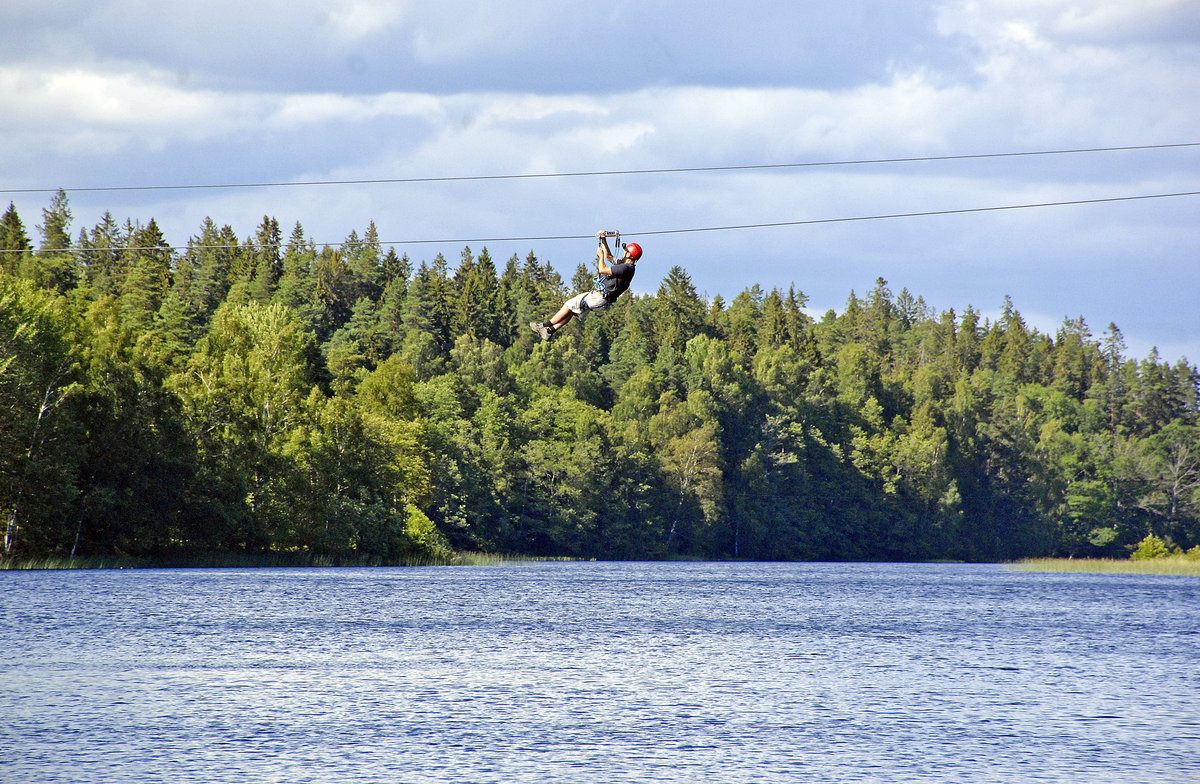 Ein Zipliner fährt über dem Sörsjön nördlich von Norrköping in Schweden. Im Hintergrund ist der Wald von Bykesbergen (126 Meter) zu sehen. Aufnahme: 21. Juli 2017.