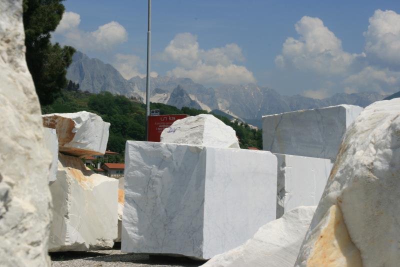 Mramorblcke roh und geschliffen. Im Hintergrund die Cave di Carrara.