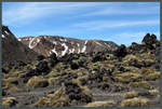 Dunkles Vulkangestein am Rand des Mount Ngauruhoe. Im Hintergrund der Red Crater, ein weiterer Vulkan des Tongariro-Massivs. (18.10.2016)
