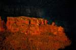 Eine Felsformation im Grand Canyon leutet blutrot im Schein der untergehenden Sonne auf.