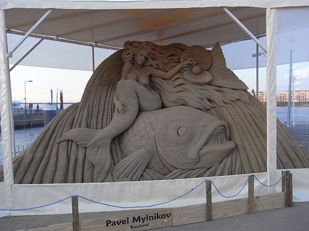 1. Warnemnder Sandwelt, Ausstellung von Internationalen Knstlern die Sandfiguren fertigen. Um die Figuren wurden Zelten aufgestellt um diese vor Regen zu schtzen. Standort ist Warnemnde direkt neben dem Fhranleger nach Hohe Dne, auf dem zum Erdbeerhof  Karl´s  gehrendem Gelnde.
Rechts im Bild, durch´s Zelt blickend, die Yachthafenresidenz Hohe Dne.