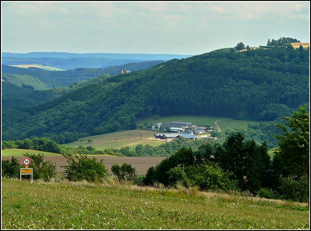 Auf diesem Bild wird die gewhnliche Perspektive, die wir als Bahnfotografen von dieser Landschaft haben, auf den Kopf gestellt. Links unten im Tal befindet sich die Haltestelle Goebelsmhle, das groe landwirtschaftliche Anwesen ist der  Fitschterhaff  und dieser befindet sich genau ber dem Portal des gleichnamigen Tunnels und man sieht auerdem, dass die Burg Bourscheid nicht auf der hchsten Erhebung dieser Region liegt. Das Bild wurde am 01.08.2010 in Schlindermanderscheid aufgenommen. (Jeanny) 