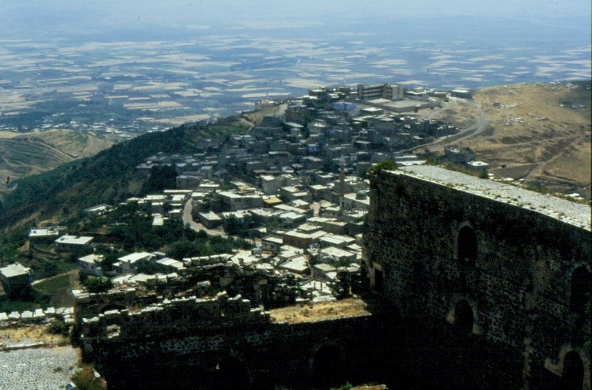 Blick ber das unterhalb der Kreuzritterburg Crac des Chevaliers liegende Dorf auf die Ebene am Fu des Alawitengebirges in Syrien (Dia vom Mai 1989). Detailfotos vom Crac des Chevaliers unter Stdtefotos.