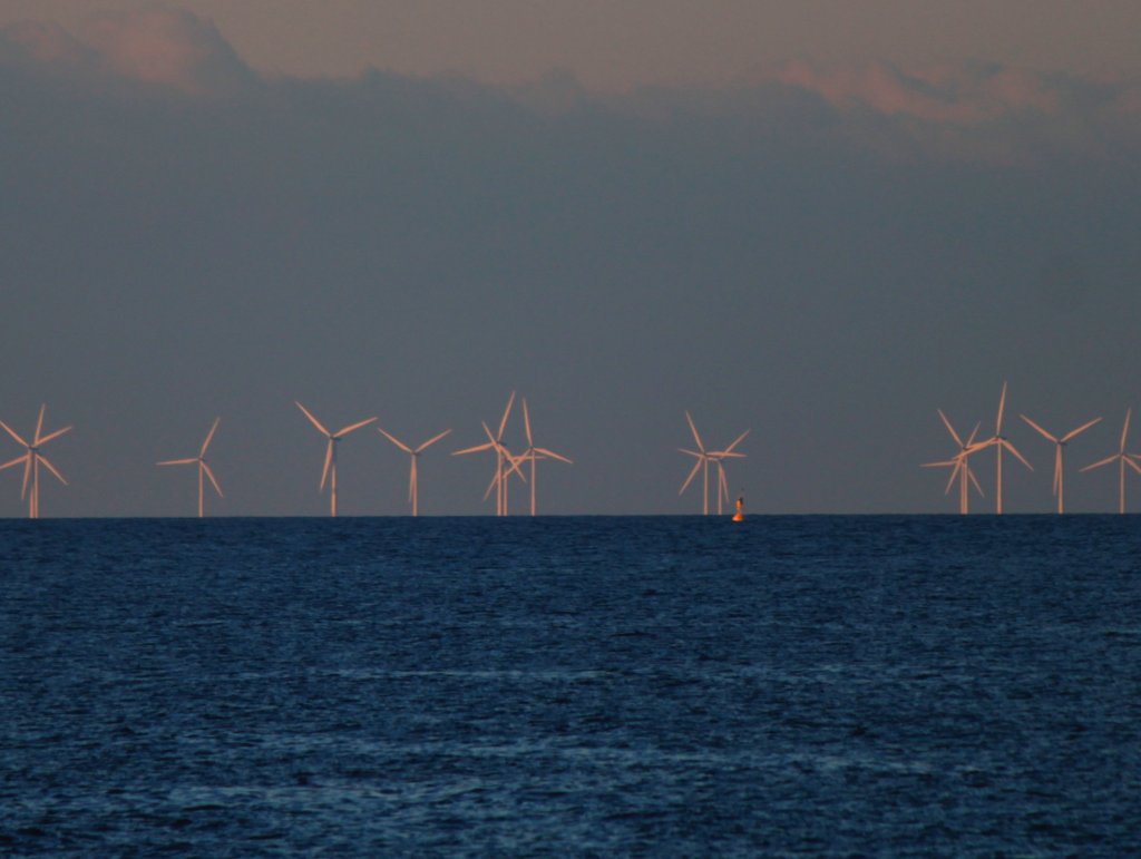 Saubere Energiegewinnung im Licht der untergehenden Sonne.
Am rande des Fehmarnbelt zwischen der Insel Fehmarn und der dnischen Insel Lolland befindet sich etwa zehn Kilometer sdlich von Nysted der Offshore Windpark Rdsand I. Hier stehen auf einem Gebiet von 24 km 72 Windkraftanlagen die eine Leistung von 166 MW haben. Die Trme sind 69 Meter hoch, die drei Rotorbltter je 41 Meter lang. Allein das Fundament jeder dieser Windkraftanlagen wiegt 1800 Tonnen, weitere 250 Tonnen wiegen der Turm mit dem Maschinenhaus, dem Generator und den Rotorblttern. Der Bau des Windparks kostete ca. 213 Millionen Euro und wurde in den Jahren 2002 bis 2004 ausgefhrt.
Aufnahme vom 08.06.2013 von der Mole des Fhrhafen Puttgarden auf Fehmarn.