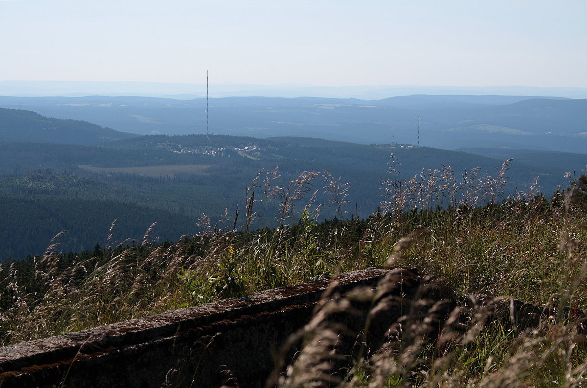 Berge des westlichen Oberharzes mit Torfhaus und seinen riesigen Antennen im Gegenlicht der Nachmittagssonne; im Hintergrund geht der Blick bis zu den 70 - 80 km entfernten Weserberglandschaften Solling und Vogler. Aufnahme vom 21. Juli 2013 auf dem Gipfelrundweg des Brocken