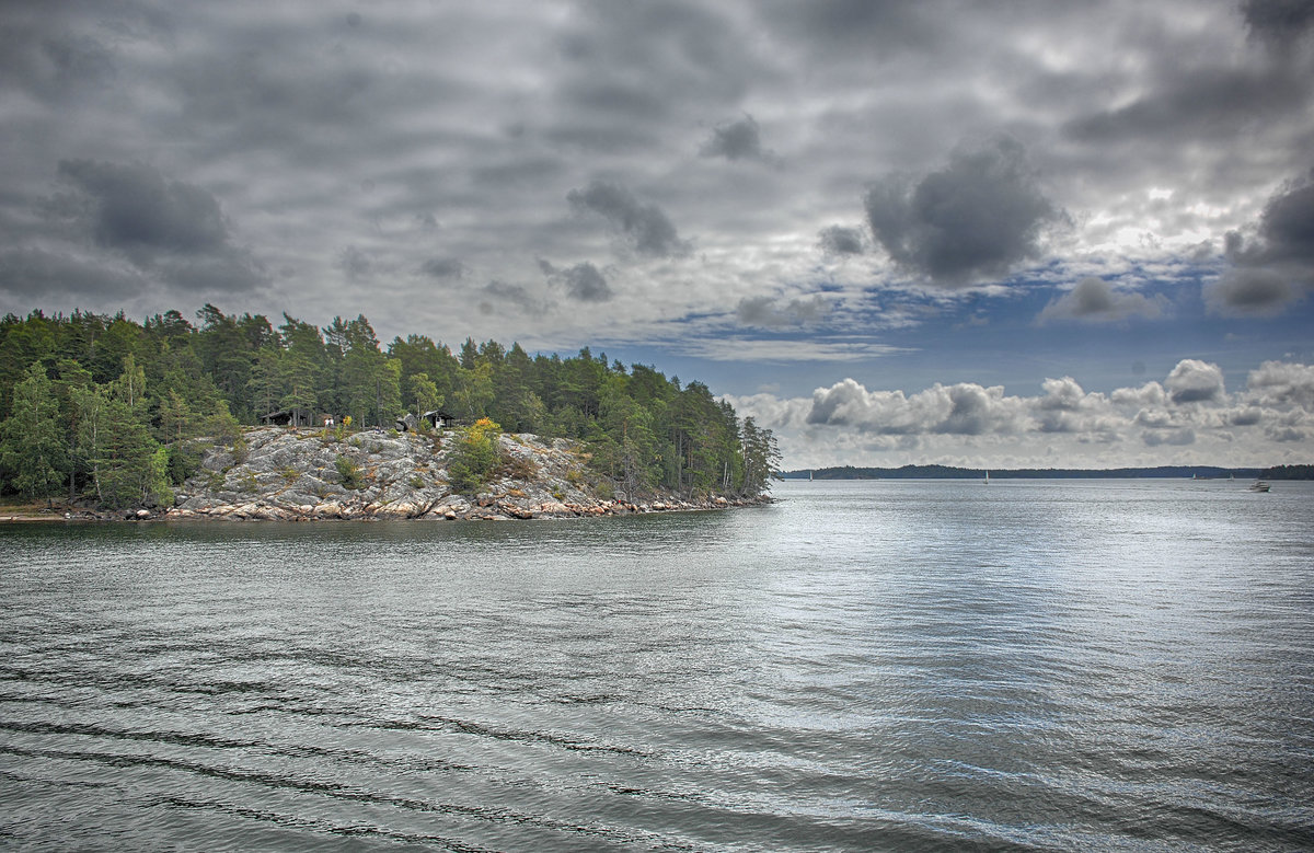 Blick auf die Insel Grind im Stockholmer Schärenhof. Schären heißen auf schwedisch skär und beschreiben eine Klippe, die aus dem Wasser schaut. Dies kann auch eine kleinere Klippeninsel oder aber eine felsige Insel im Meer sein. Viele Schären bilden einen skärgård, was soviel wie Schärenhof bedeutet. Wegen der klanglichen Nähe und der romantischen Vorstellung, die man mit einem Garten verbindet wurde aus gård – Garten. Deshalb sagt man auf Deutsch jetzt Schärengarten.
Aufnahme: 26. Juli 2017.