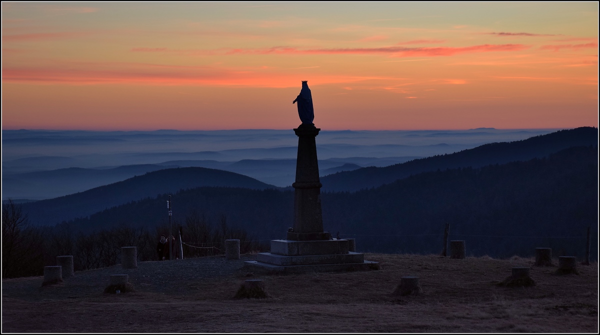 Blick vom Elsässer Belchen in den Burgund. Dezember 2016. Nicht ganz einfach ist die Verortung der Kategorie... Steht der Fotograf im Departement Haut-Rhin, hinter der Marienstatue ist das Territoire de Belfort, ganz rechts das Departement Vosges und im  blaue leuchtenden Tiefland dürften gleich die drei Departements Haute Saône, Doubs und Jura zu sehen sein.