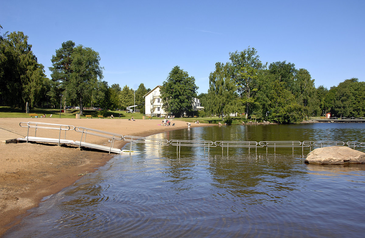 Der Strand »Evedalsbadet« am Halgasjön nördlich von Växjö in Småland / Schweden. Im Hintergrund ist die Jugendherberge von Växjö zu sehen. Aufnahme: 20. Juli 2017.