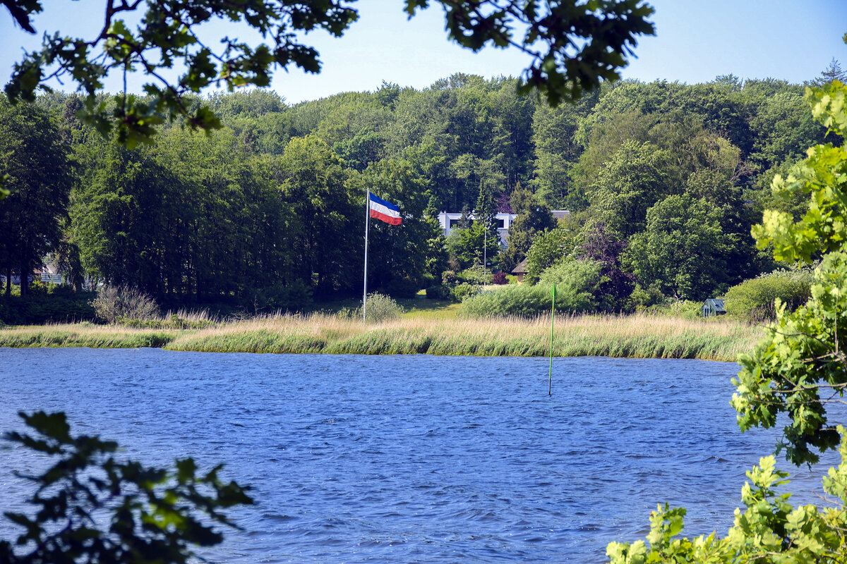 Die Schleswig-Holstein-Flagge weht auf einem Grundstück in Wassersleben. Im Vordergrund ist die Flensburger Förde zu sehen. Aufnahme: 11. Juni 2023.