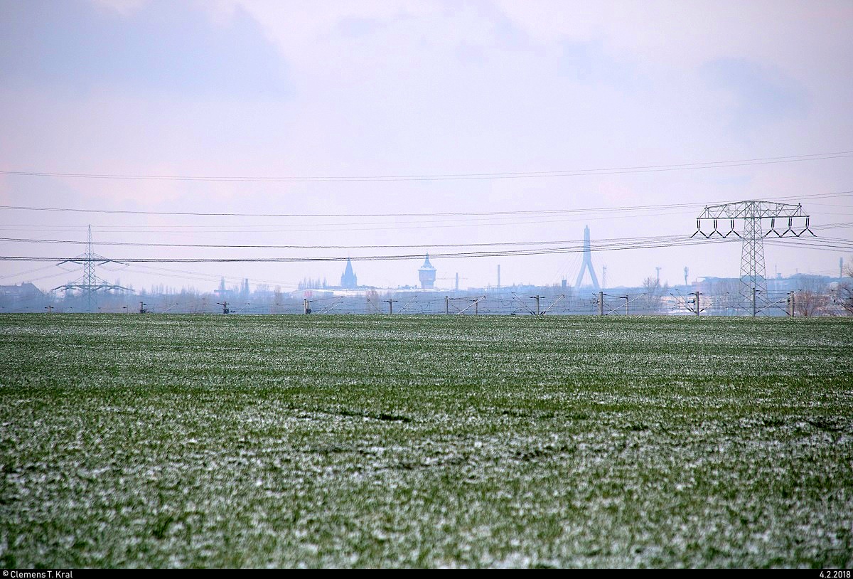 Hinter dem Acker und der Neubaustrecke Erfurt–Leipzig/Halle bei Benndorf (Gemeinde Kabelsketal) erkennt man imposante Silhouetten. Es handelt sich um Gebäude der Stadt Halle (Saale).
V.l.n.r.: Pauluskirche, Wasserturm Nord, Pylon der Berliner Brücke. [4.2.2018 | 11:05 Uhr]