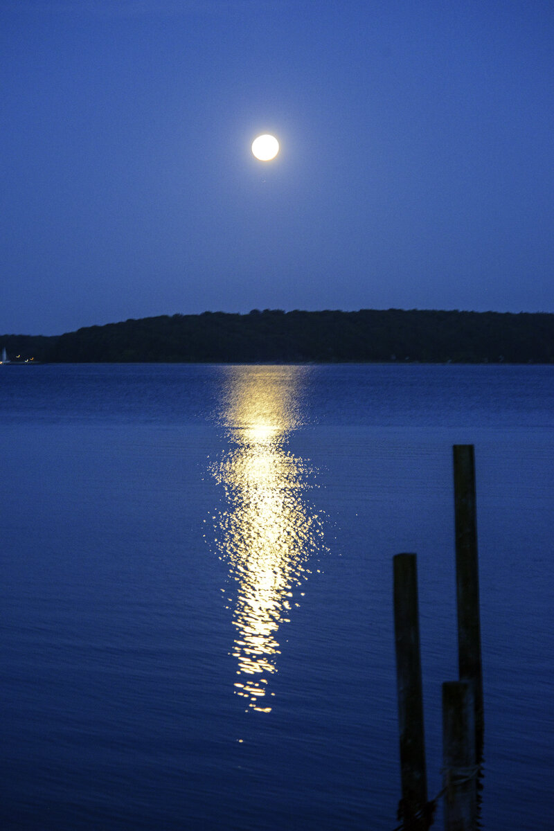 Mondlicht über der Flensburger Förde. Das Bild wurde von der dänischen Seite der Förde aus aufgenommen.  Auf der anderen Seite des Fjords kann man die Waldgebiete bei Glücksburg sehen. Aufnahme: 3. Juni 2023.