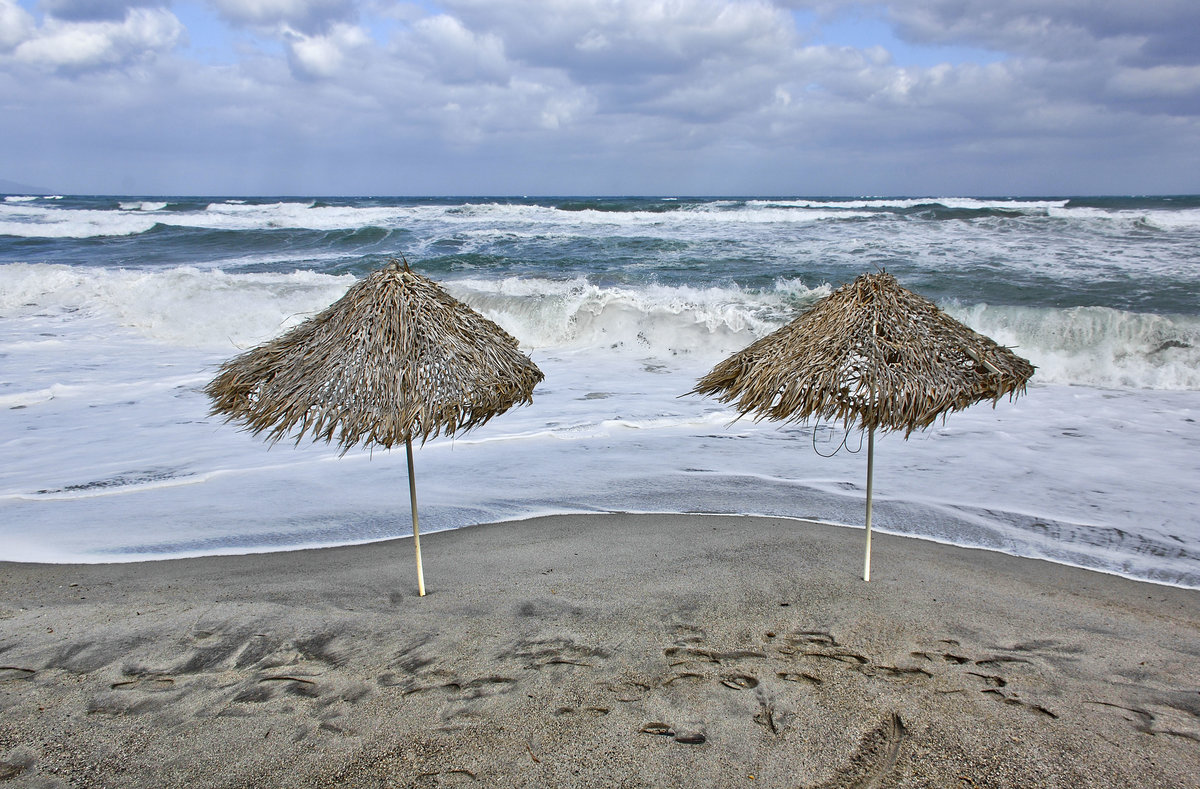 Sonnenschirme am Strand vor Geranie auf Kreta. Aufnahme: 18. Oktober 2016.