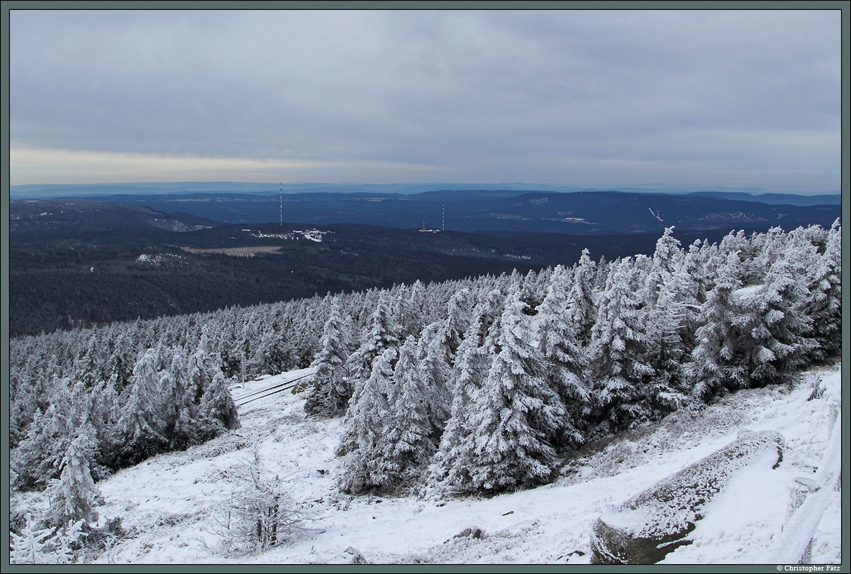 Trotz des frostigen und trüben Wetters bot sich am 27.12.2014 von Brocken ein guter Weitblick in Richtung Westharz. In der Bildmitte befinden sich die Lerchenköpfe, auf deren zwei Kuppen sich die Funktürme des Senders Torfhaus befinden. Am Fuße des linken Senders befindet sich die kleine Siedlung Torfhaus, die vor allem als Ausflugsort und Ausgangspunkt für Wanderungen dient. Links im Vordergrund taucht zwischen den Bäumen kurz die Strecke der Brockenbahn auf, die seit 1898 bis zum Brockengipfel führt.