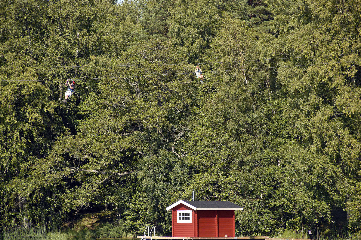 Zwei Zipliner über der Sörsjön nördlich von Norrköping in Schweden. Im Wald befindet sich der Kletter- und Abenteuerpark Sörsjöns Äventyrpark. Aufnahme: 21. Juli 2017.