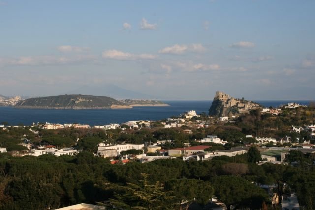 Blick ber Ischia zur Isola di Prchida. Rechts im Vordergrund sieht man das Wahrzeichen der Altstadt von Ischia, das Castello von Ischia Ponte. Im Hintergrund erkennt man am Ende vom Golf di Napoli schwach den Vesuv.