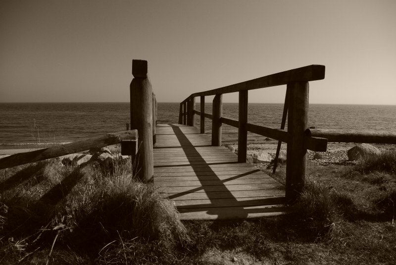 Licht und Schatten auf einer Holzbrcke an den Strand. Eingefangen in einem Ensemble aus Grautnen