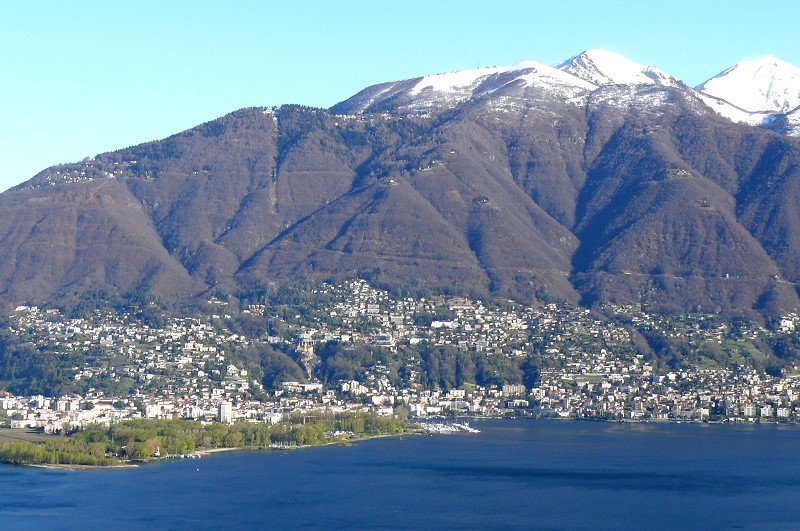 Piazoggna - Blick ber den Lago Maggiore auf Locarno (links), Orselina (Mitte oben) und Muralto (rechts). Ab Orselina fhrt eine 2050m lange Seilbahn ber 915 Hhenmeter auf Gardada und ab da ein 915m lange Sesselbahn ber 314 Hhenmeter auf Cimetta (1660m, noch schneebedeckt) - Foto vom 07.04.2008