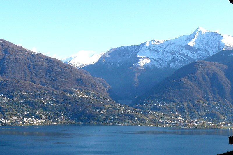 Piazoggna - Blick ber den Lago Maggiore auf Minusio, Contra (links vom Staudamm, Tenero (unterhalb Staudamm) und Gordola (rechts). Die 220m hohe Staumauer Selvatica staut die Verzasca.  Das Verzascatal ist sicher dasjenige, das von den Tlern sdlich der Alpen am besten seine Ursprnglichkeit bewahren konnte, liegt ziemlich zentral im Tessin und ist nur von Tessiner Tler umgeben. Rechts ist die schneebedeckte Pyramide des Piz Vogorno (2360m) zu sehen - Foto vom 07.04.2008   