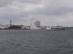 Blick auf Warnemnde mit Leuchtturm, Teepott, Hotel  Neptun  und das neu aufgestellte Riesenrad direkt am Strand.
Im Vordergrund das Fahrgastschiff  Rostocker7  beim eindrehen zum AltenStrom in Warnemnde.
Bereits am Liegeplatz fest das Fahrgastschiff  Baltica 