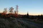 Rot glüht die untergehende Sonne auf Bäumen und buntem Laub an der Hahnenkleer Waldstraße; im Hintergrund Berge im Südharz und jenseits des Odertals; Sonntag, 24.10.2021...