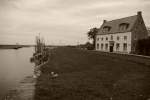 Ostfriesland in Schwarzweiss: In Grautnen wirkt das Haus mit dem kleinen Anleger vor der Tr noch einsamer im Zusammenspiel mit Himmel und Wolken.