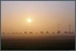 Langsam löst sich am 21.08.2015 der Morgennebel auf, als sich die aufgehende Sonne über die Felder und Windräder bei Eilvese erhebt. 