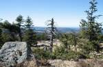 Vorfrhling auf dem Brocken: Blick um die Mittagszeit des 25.03.2012 vom Gipfelrundweg des Brocken Richtung Westen in seine Urwaldvegetation mit einem abgebrochenen Baum und einem von Flechten berwachsenen Felsblock. Im Hintergrund hinter den Bumen kann man Berge des westlichen Oberharzes mit dem ber 900 m hohen Bruchberg erkennen.