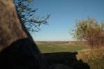 Inmitten der weiten Landschaft mit Feldern, sanften Bergreihen und Obstbäumen steht in der Ferne die Windmühle von Warnstedt.