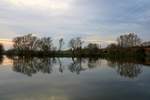 Die Bäume an der Saale in der Saaleaue bei Böllberg-Wörmlitz in Halle (Saale) sind Anfang November fast kahl und spiegeln sich im ruhigen Fluss neben der Bahnstrecke Halle–Hann.