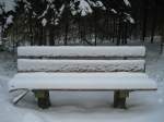So einsam und allein stand diese verschneite Bank im Wald

