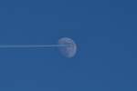 Flugzeug mit Kondensstreifen vor zunehmenden Mond.