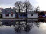 Die alte Bahnmeisterei am Rieder Bahnhof, sowie die dahinter liegenden Platanen spiegeln sich in einer Wasserlache;120102